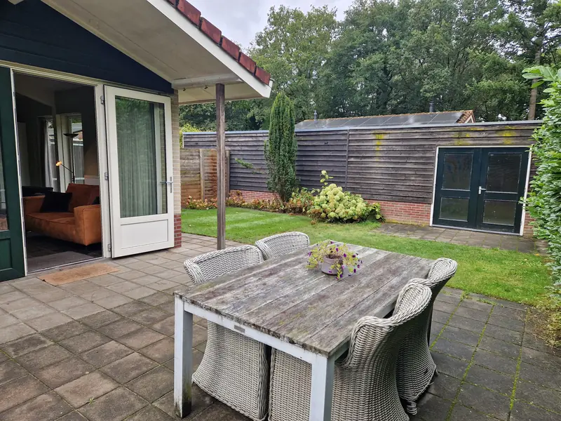 Het terras van huisje&nbsp;2 met een tafel en zes stoelen, en achter het gras de schuur.
