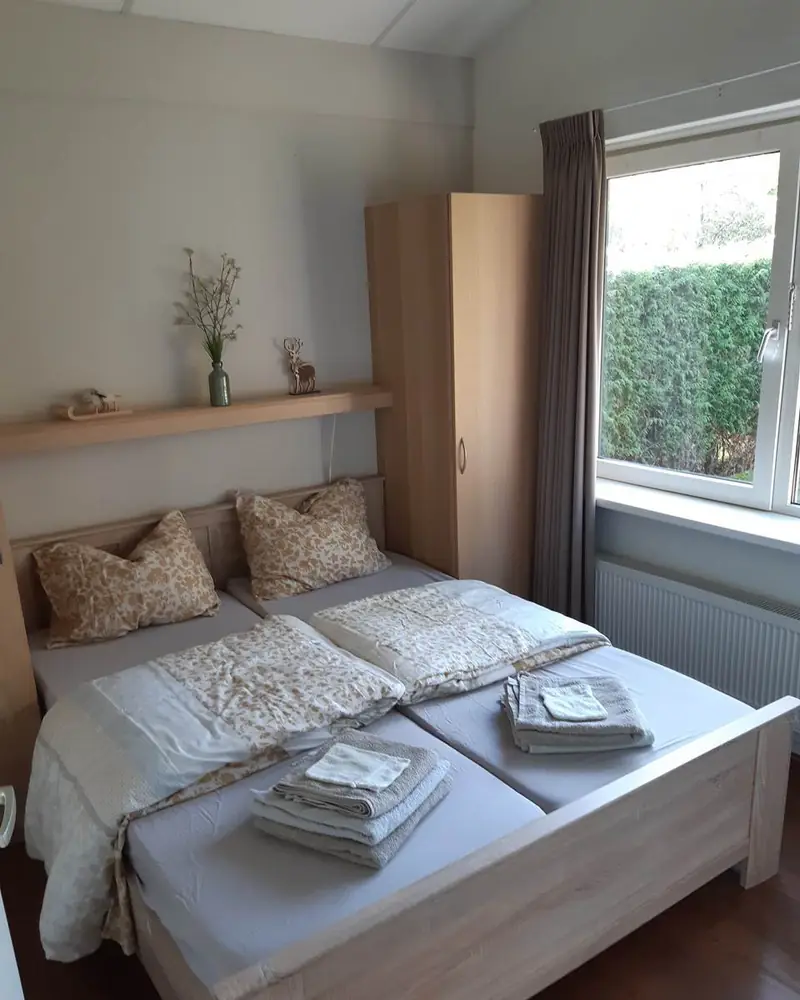 De eerste slaapkamer van huisje&nbsp;3, met het tweepersoonsbed en het raam met uitzicht op de haag.