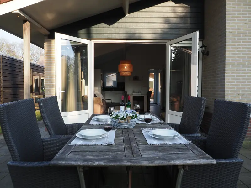 Het terras van huisje&nbsp;3: de gedekte tafel voor de openslaande deuren, en in de woonkamer de rotan hanglamp.