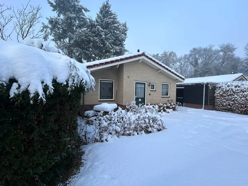 De voorkant van huisje&nbsp;3 in de winter, met sneeuw op de oprit en de haag.
